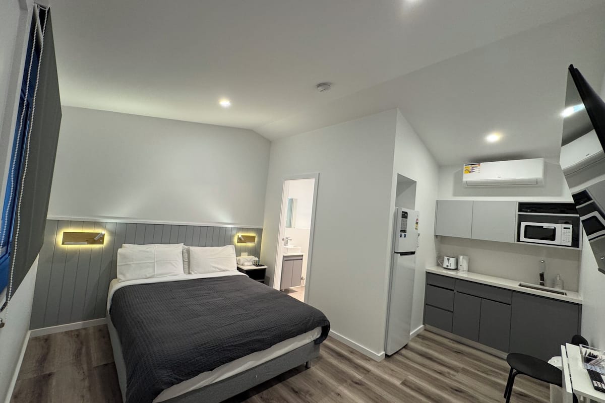 Een kleine hotelkamer met een bed, nachtkastje en een kitchenette, inclusief een magnetron en koelkast.