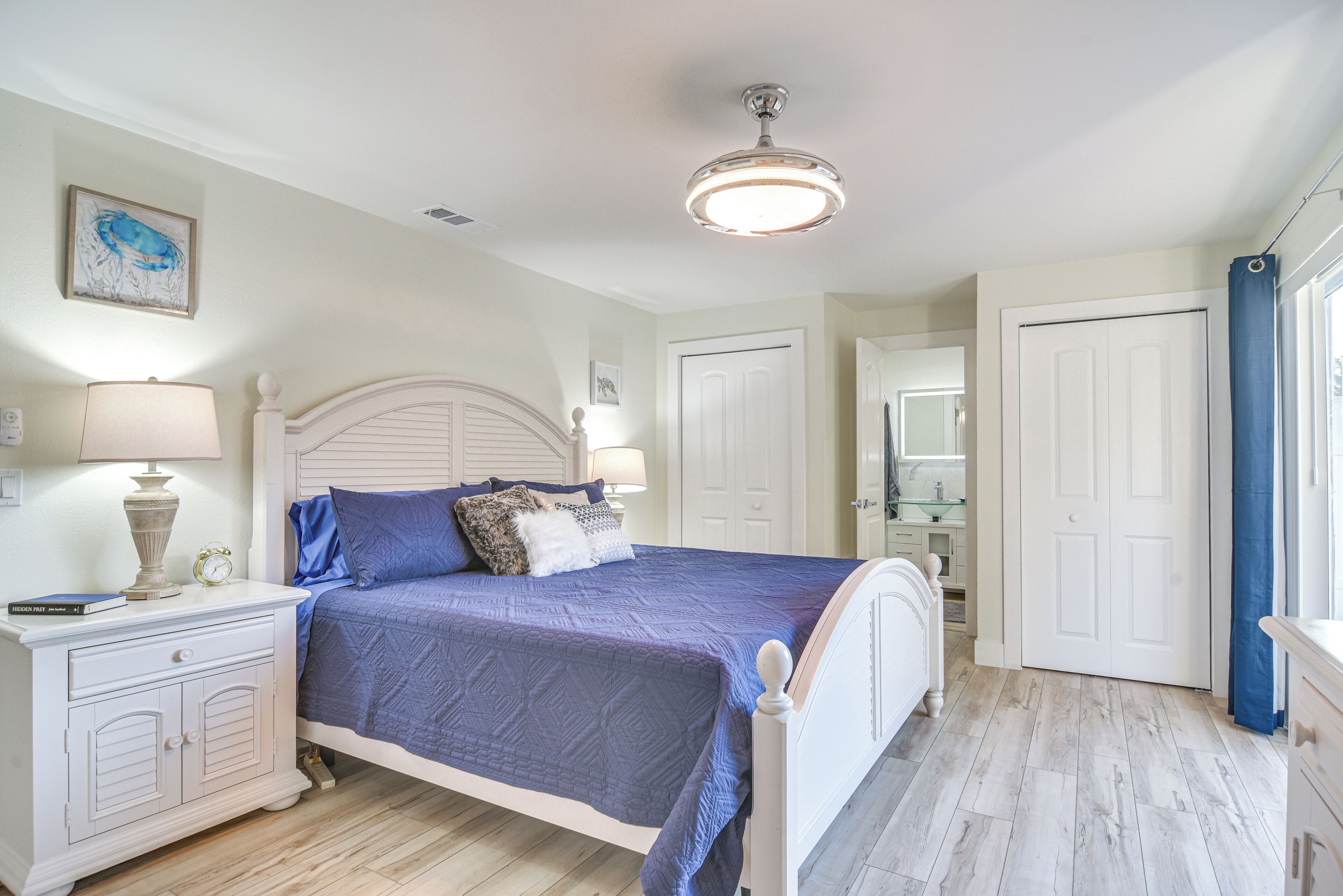 A bedroom with a bed, nightstands, a ceiling fan, and a door.