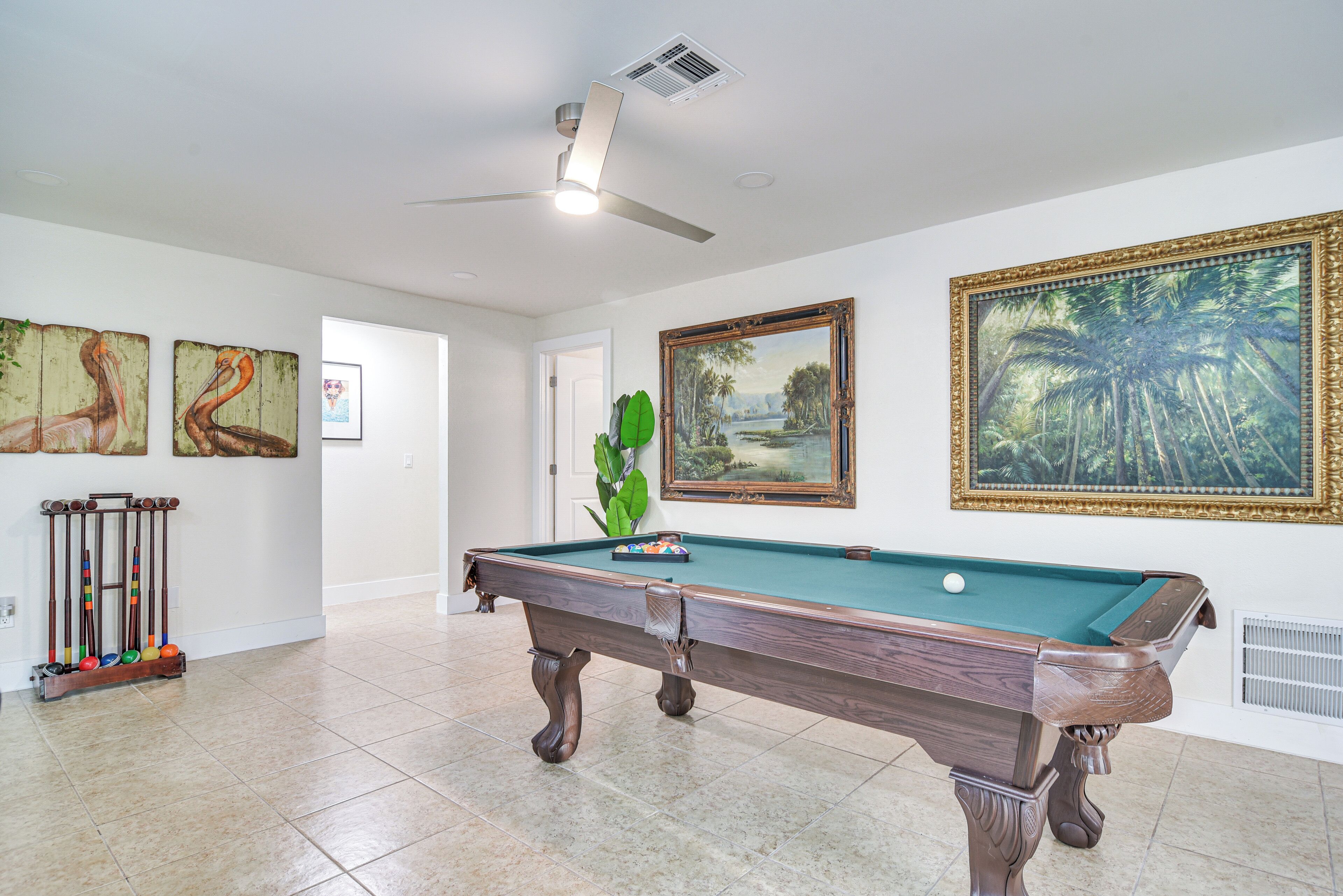A pool table in a room with white walls, a ceiling fan, and framed artwork.