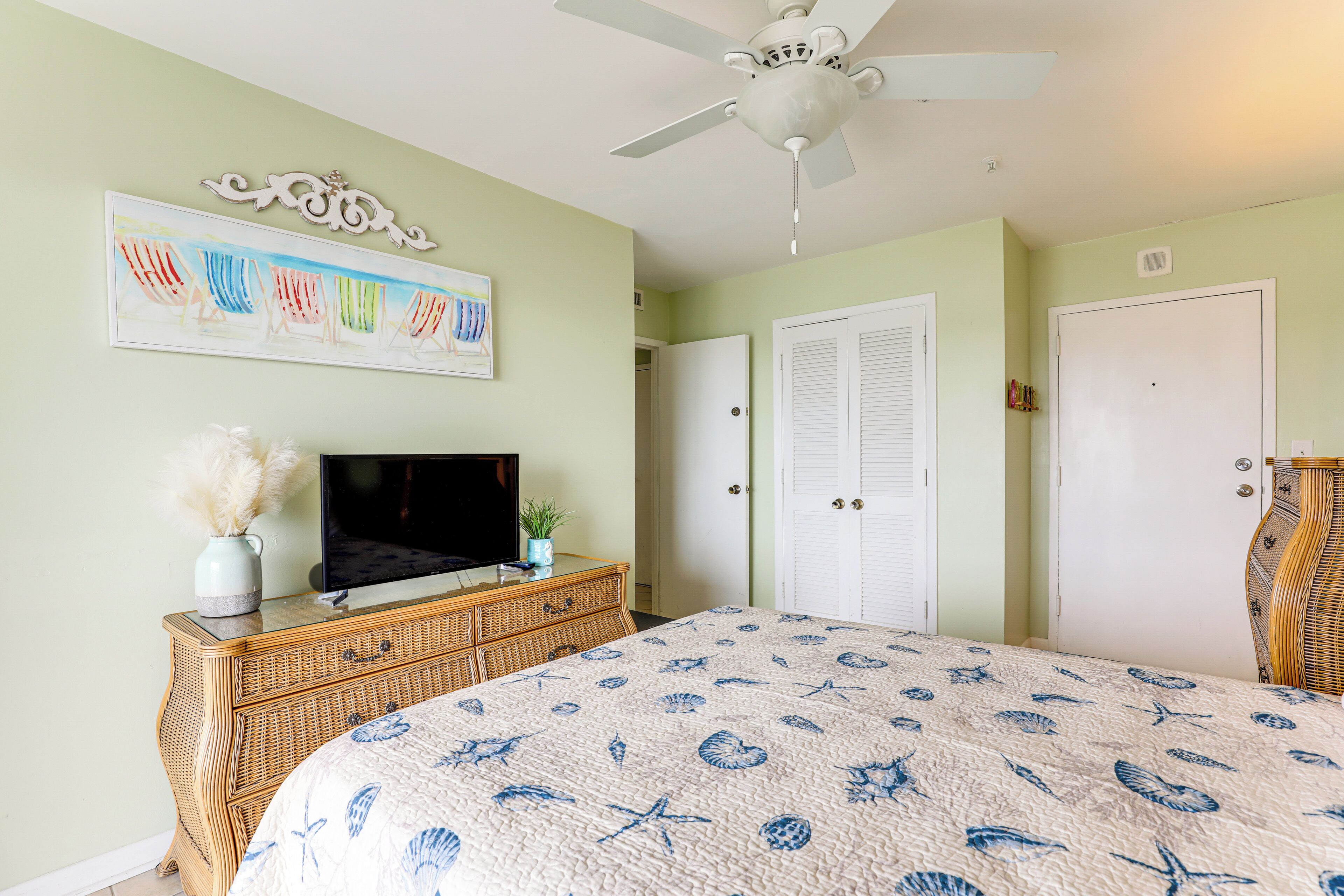 A bedroom with a bed, a television on a dresser, a ceiling fan, and a wall with a framed picture.