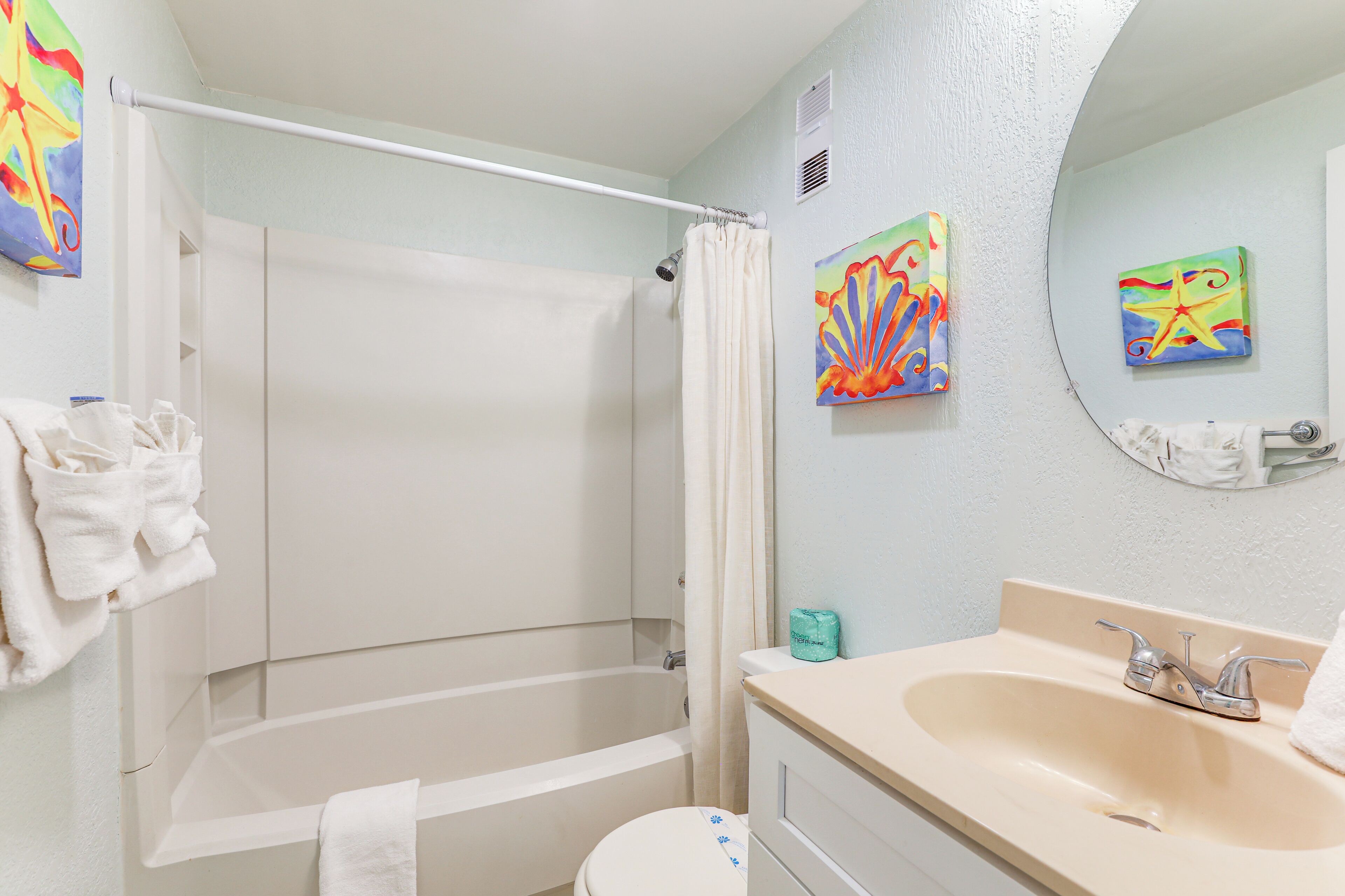 A bathroom with a bathtub, a sink, and two wall-mounted artwork pieces.