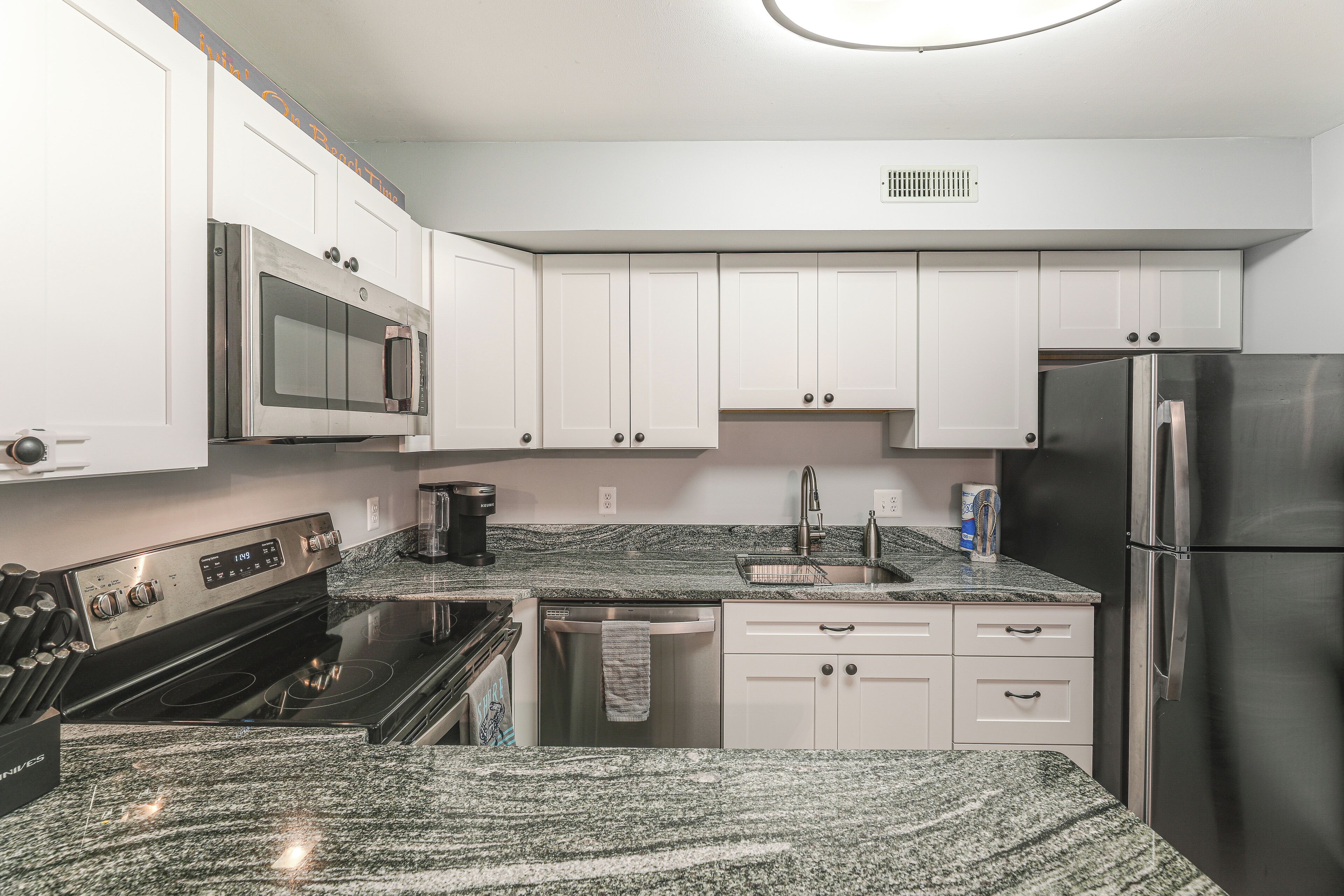 A modern kitchen with white cabinets, a stainless steel refrigerator, a built-in oven, and a granite countertop.