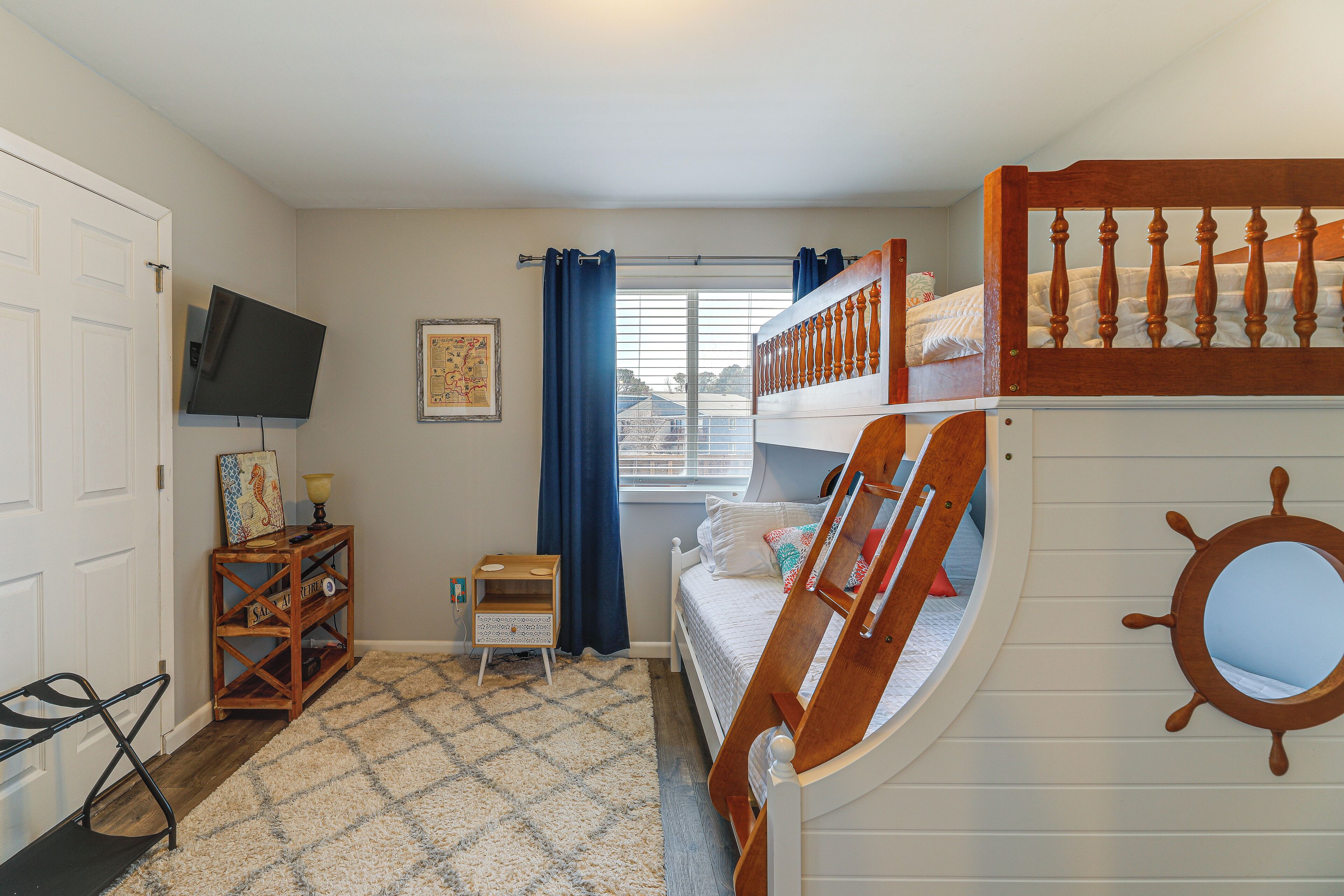 A bedroom with bunk beds, a TV, a small table, and a window with curtains.