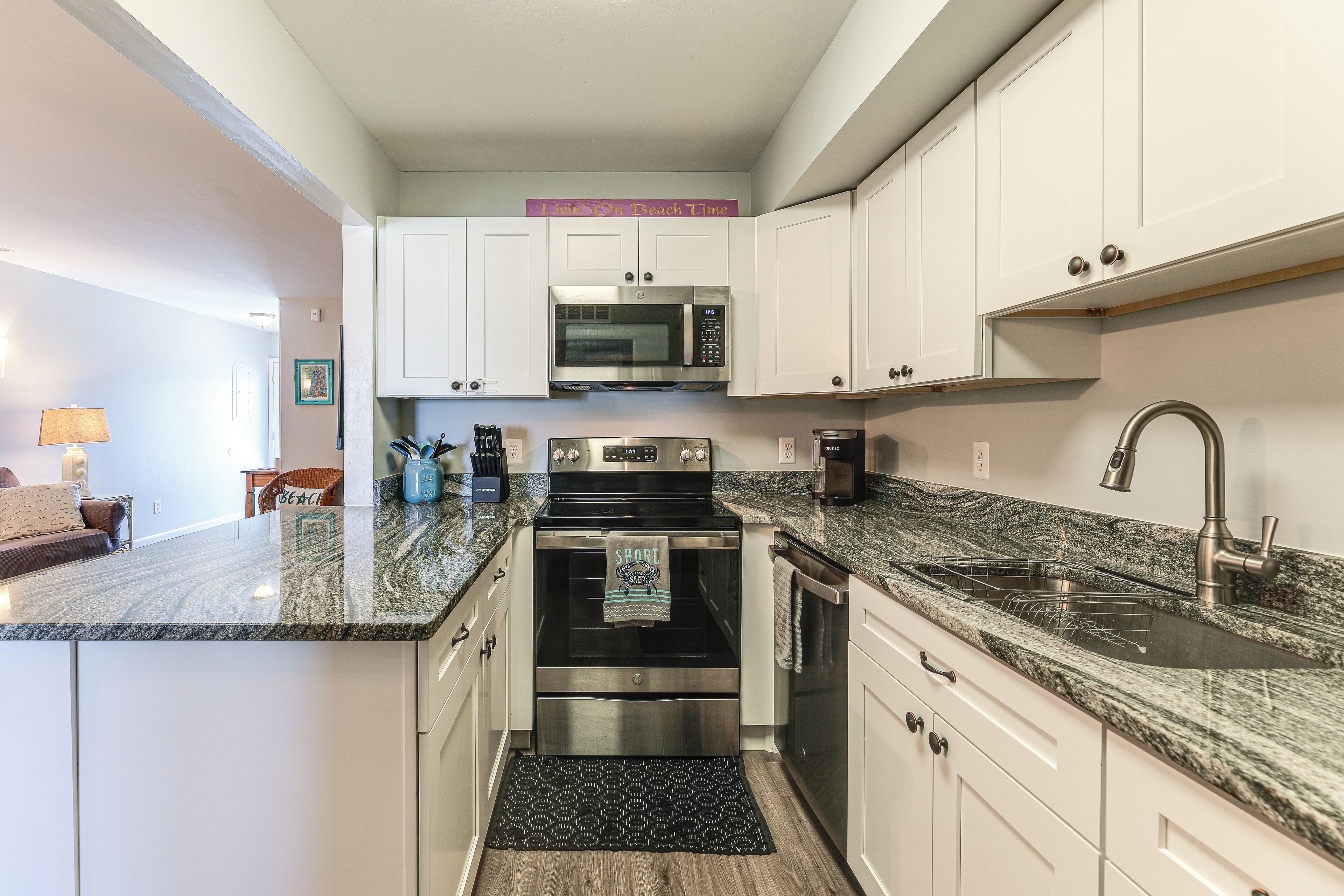 A modern kitchen with white cabinets, a stainless steel microwave, and an oven.