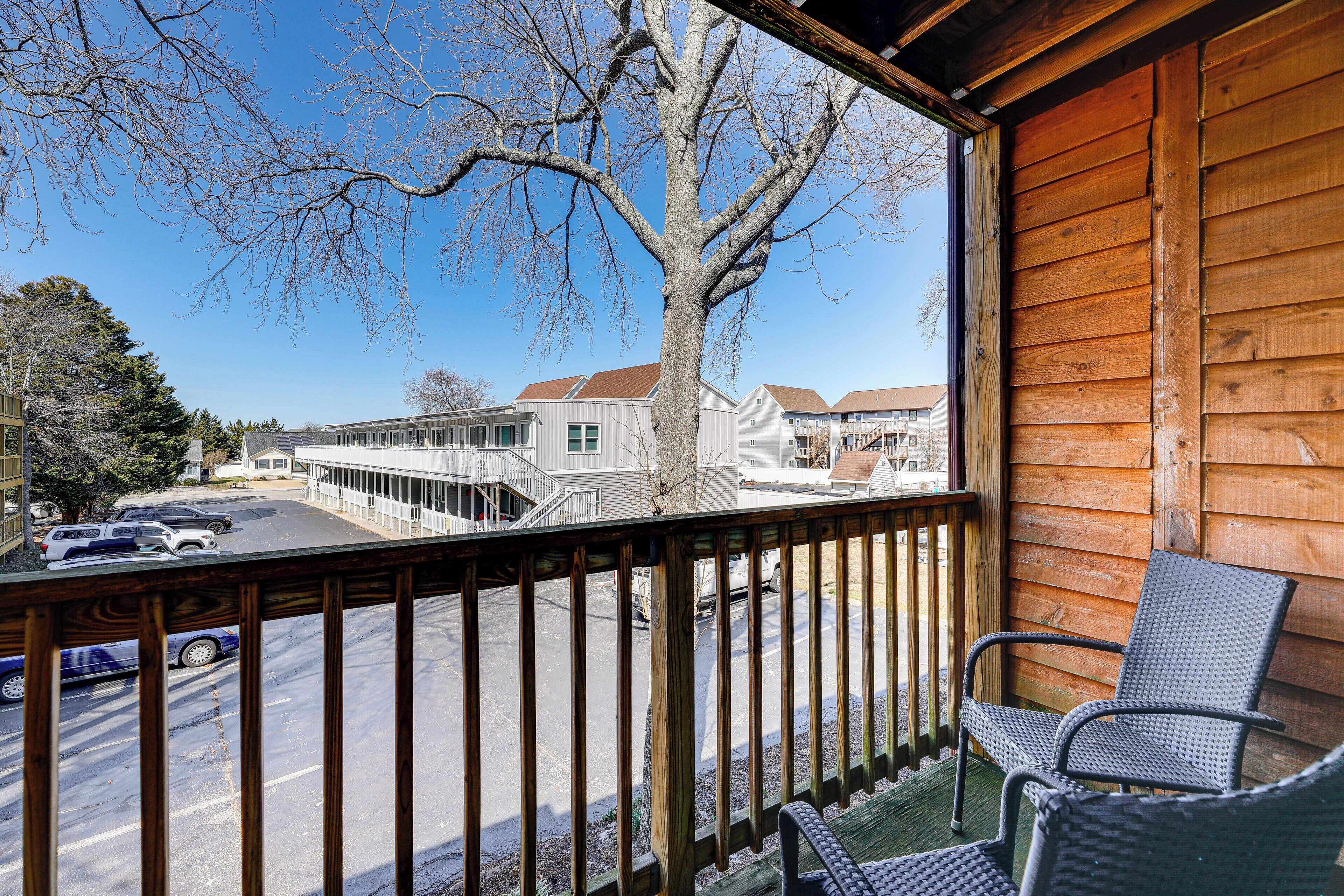 A wooden deck with a view of a street and buildings. There are two wicker chairs on the deck.