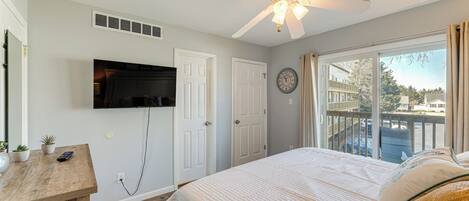A bedroom with a bed, a ceiling fan, a TV mounted on the wall, and a window with curtains.