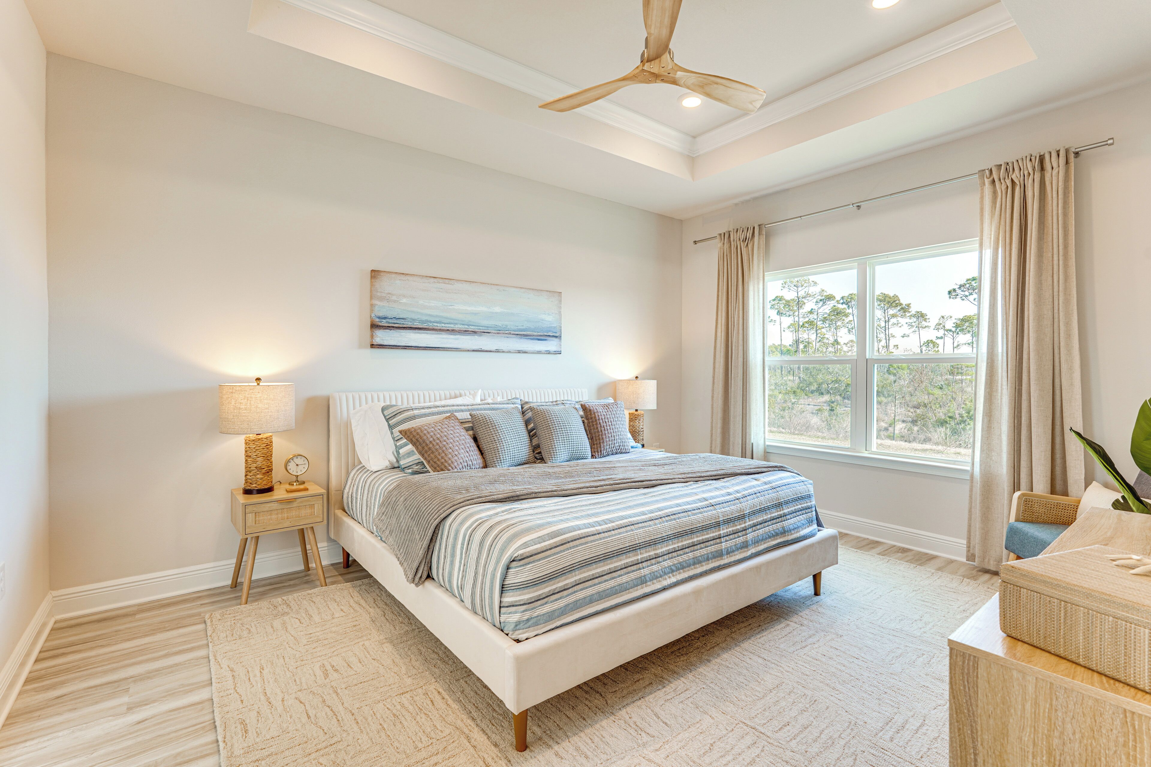Une chambre à coucher avec un lit, des lampes de chevet, un ventilateur de plafond, une fenêtre avec des rideaux et un tableau au mur.