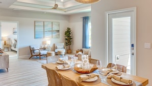 A dining area with a wooden table set for four, surrounded by wicker chairs, a ceiling fan, and a large woven light fixture.