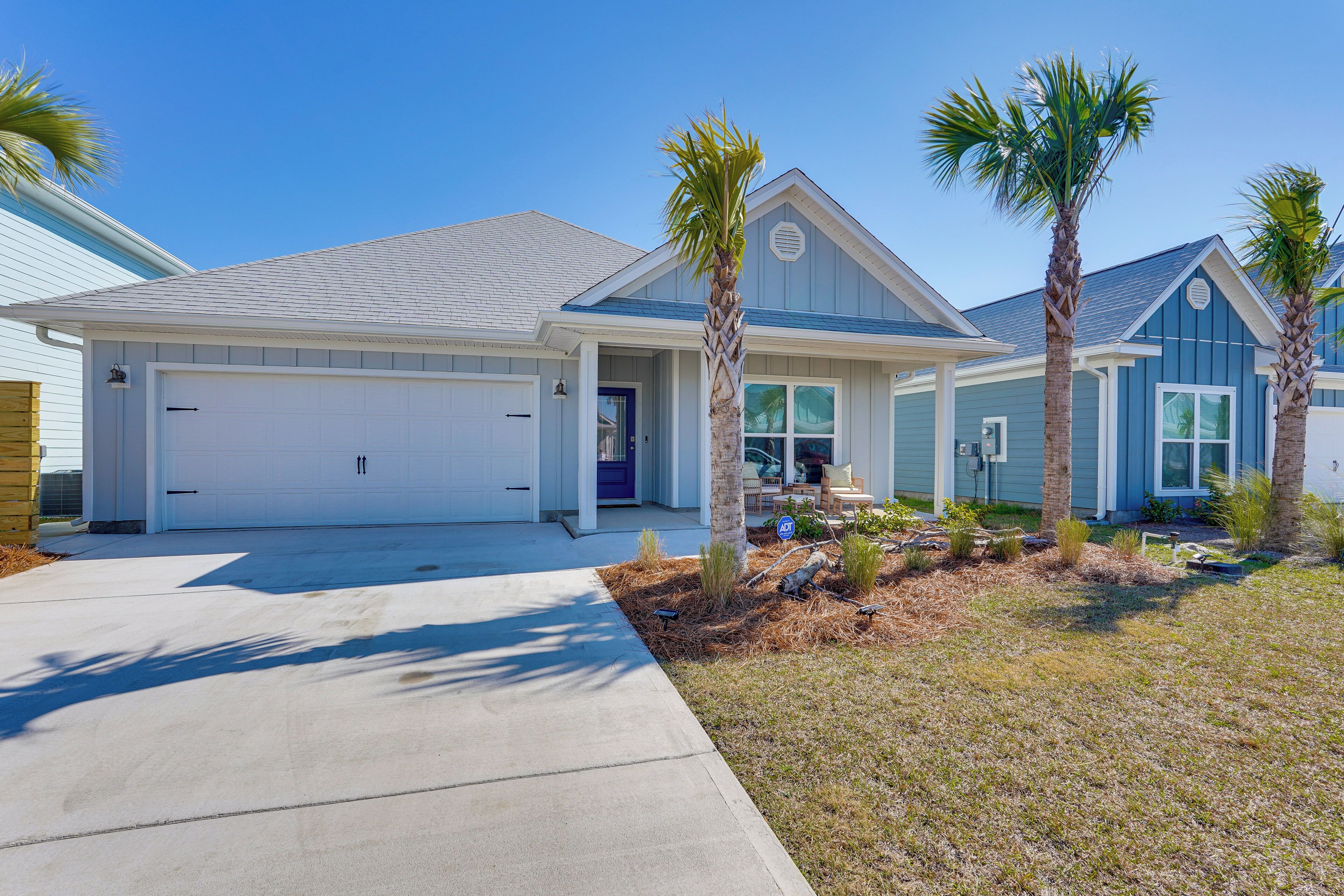 A two-story house with a garage, a covered porch, and palm trees.