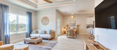 A spacious living room with a large TV, a dining area, and a cozy seating area with a sofa and ottomans.