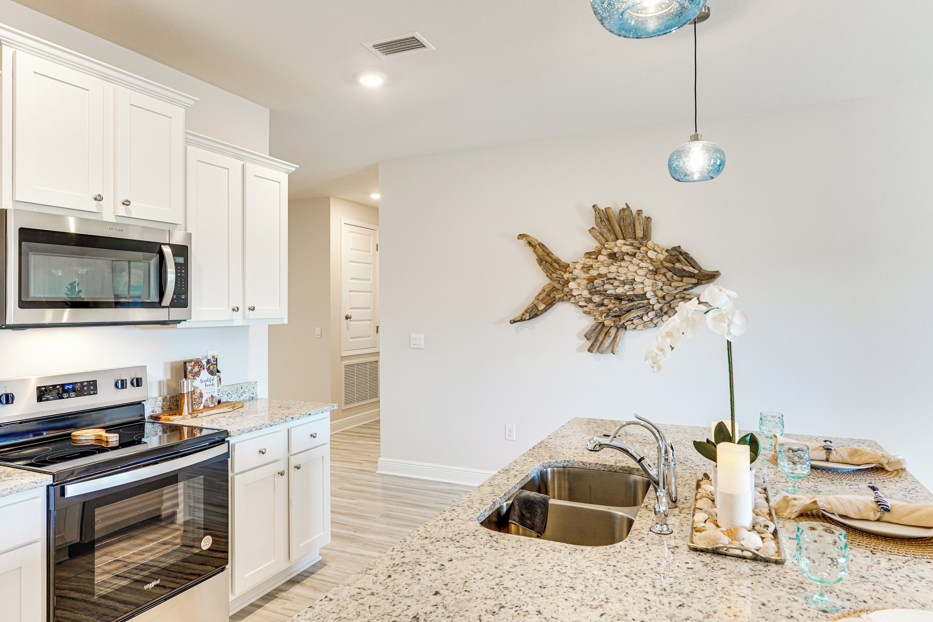 A kitchen with white cabinets, a stainless steel microwave, an oven, granite countertops, a sink, and a decorative wall piece.