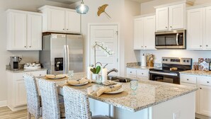 A modern kitchen with white cabinetry, a central island with seating, a built-in oven, and a microwave.