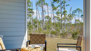 A patio with wicker chairs and a table, overlooking a forested area.