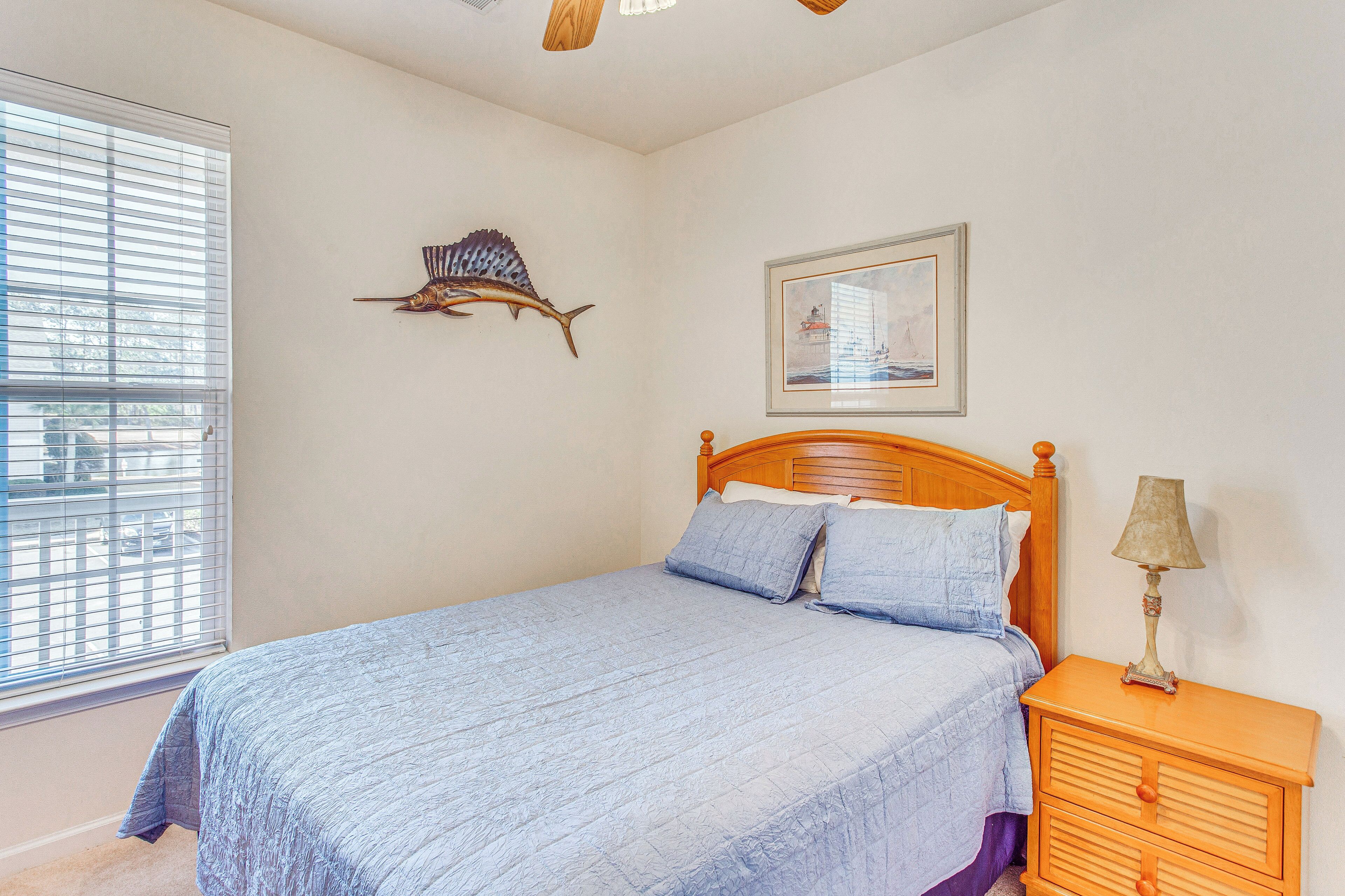 A bedroom with a bed, a nightstand, a lamp, a window with blinds, a wall-mounted fish decoration, and a framed picture.