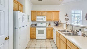 A kitchen with wooden cabinets, a white refrigerator, a microwave, an oven, a dishwasher, and a sink. - 5 Mi to Shore: Condo w/ Patio in Sunset Beach! (Sunset Beach)