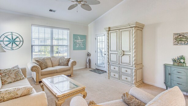 A spacious living room with a beige sofa set, a glass-top coffee table, and a large white cabinet. - 5 Mi to Shore: Condo w/ Patio in Sunset Beach! (Sunset Beach)