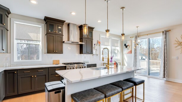A modern kitchen with dark cabinets, a large island with bar stools, and a view to the outside. - 10 Mi to Morristown: Stylish Home Near Trails! (Rockaway)