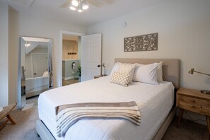 A bedroom with a large bed, a bedside table, a nightstand, a mirror, and a wall-mounted artwork.