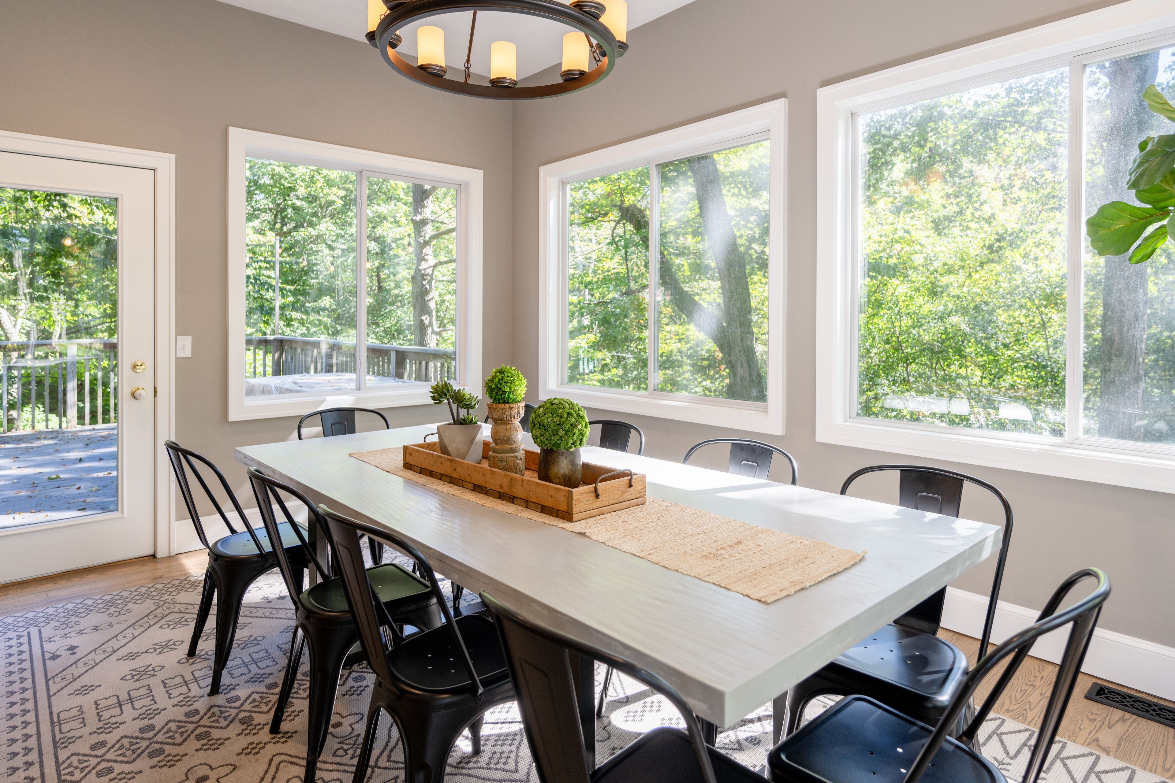 A dining area with a large table, chairs, and a view of trees through large windows.