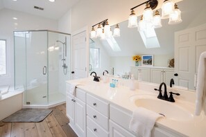 A modern bathroom with a glass shower enclosure, a large vanity with a double sink, and a skylight above the mirror.
