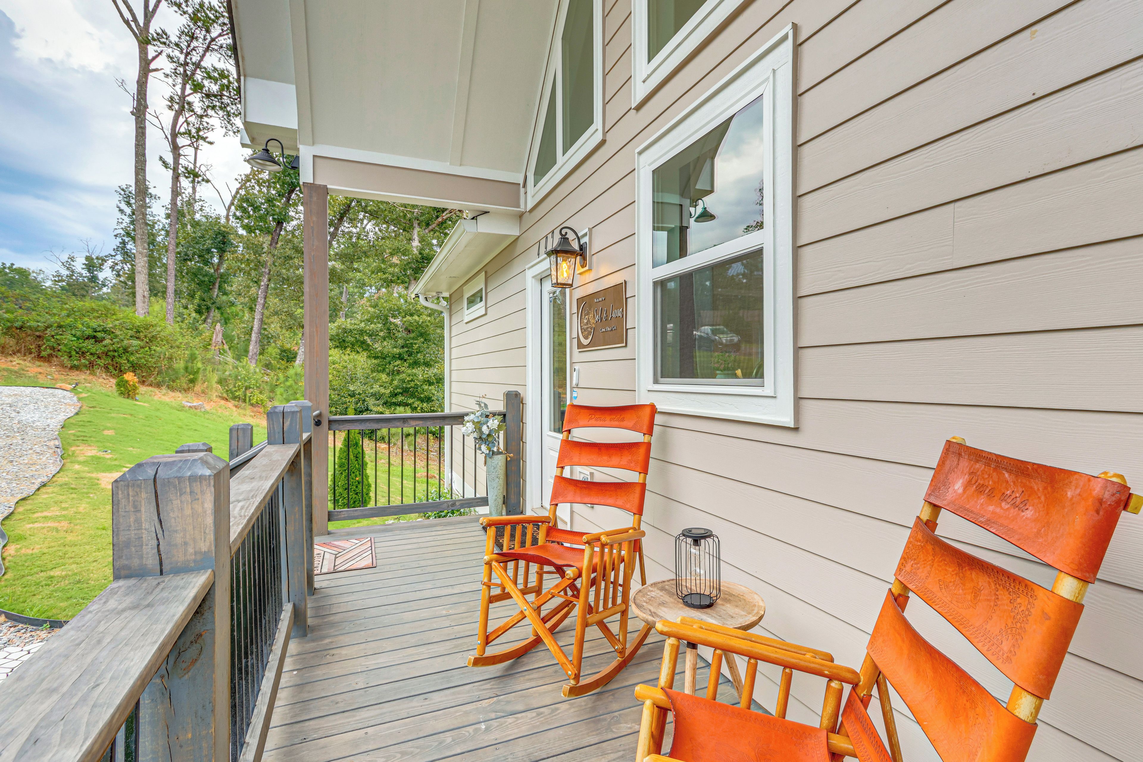 A wooden deck with two rocking chairs and a small table, overlooking a grassy area with trees.