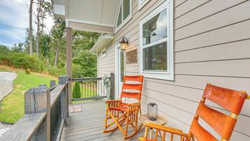 A wooden deck with two rocking chairs and a small table, overlooking a grassy area with trees.