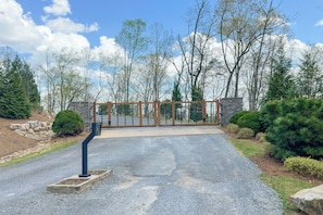A gated driveway leading to a building with a stone wall and a metal gate. - Luxury Cabin, Mountain Views, Hot Tub, EV Charger (Ellijay)
