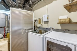 A laundry area with a front-loading washer and dryer, a utility room with a water heater, and a shelf with a towel. - Luxury Cabin, Mountain Views, Hot Tub, EV Charger (Ellijay)