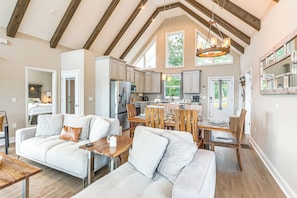 A spacious living area with a high ceiling and exposed beams, a dining area with wooden chairs and a table, and a kitchen with modern appliances. - Luxury Cabin, Mountain Views, Hot Tub, EV Charger (Ellijay)