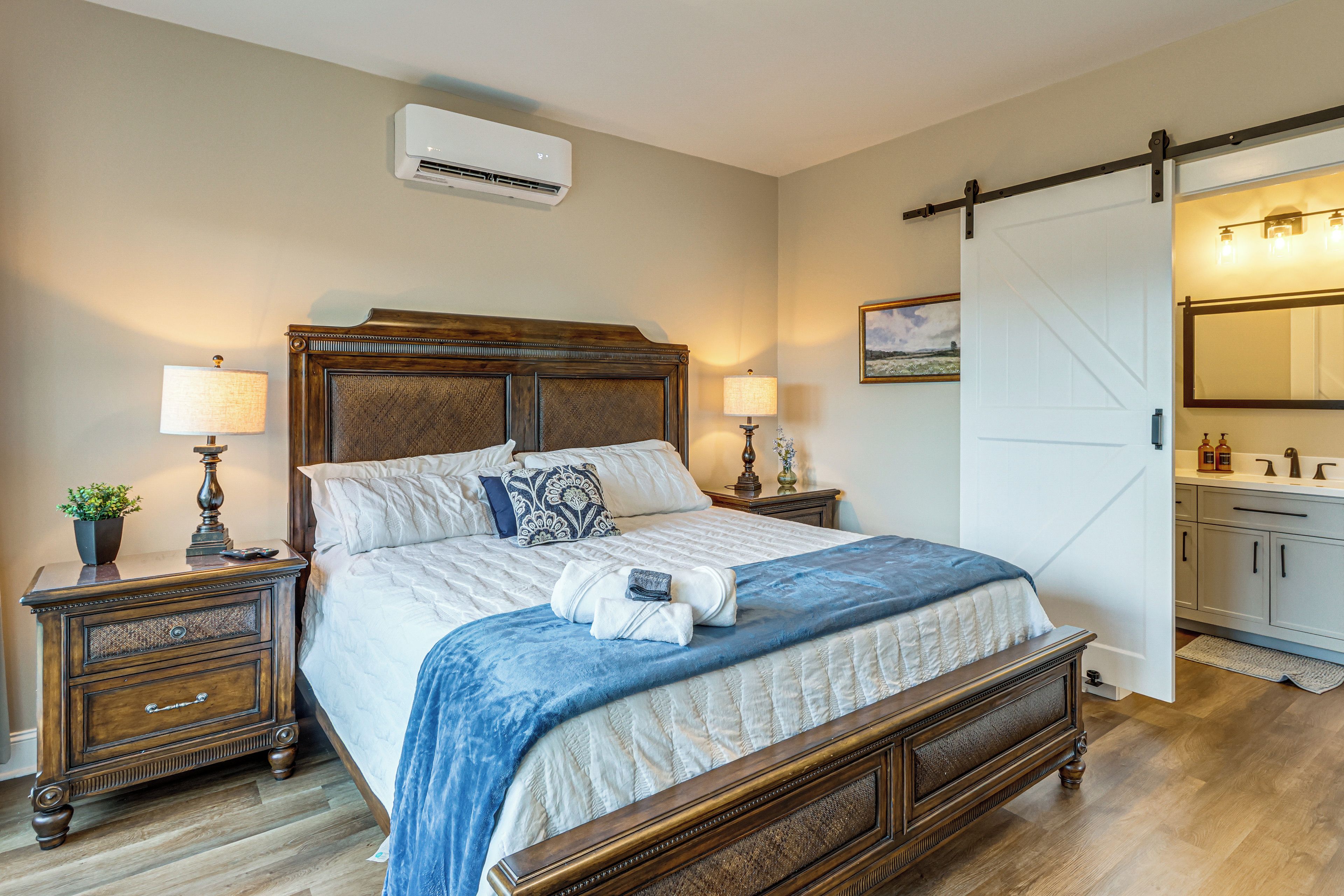 A bedroom with a large bed, two bedside tables, a dresser, a sliding barn door, and an air conditioning unit.