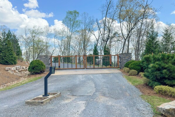A gated driveway leading to a building with a stone wall and a metal gate. - Sol & Luna: Luxury Cabin, Mountain Views, Hot Tub (Ellijay)