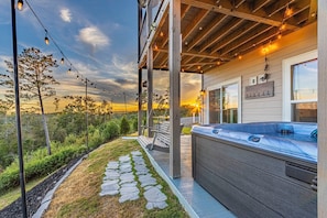 A covered outdoor area with a hot tub, stone pathway, and string lights. - Luxury Cabin, Mountain Views, Hot Tub, EV Charger (Ellijay)