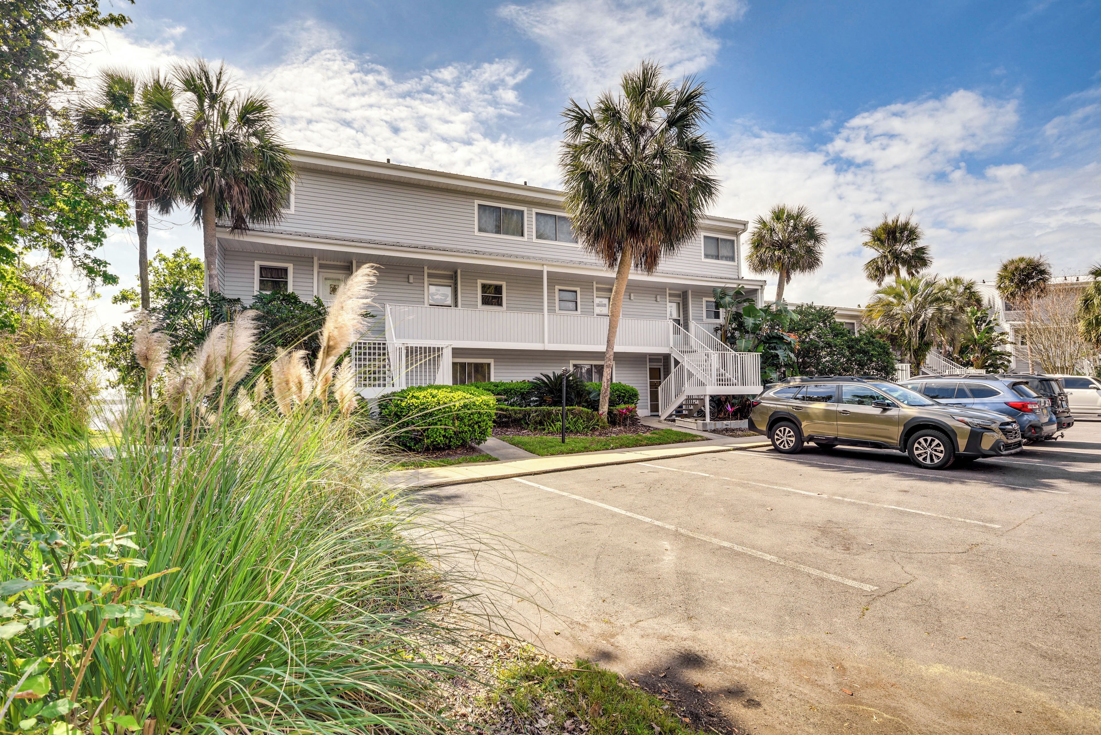 A multi-story motel with a parking lot, palm trees, and a clear sky.