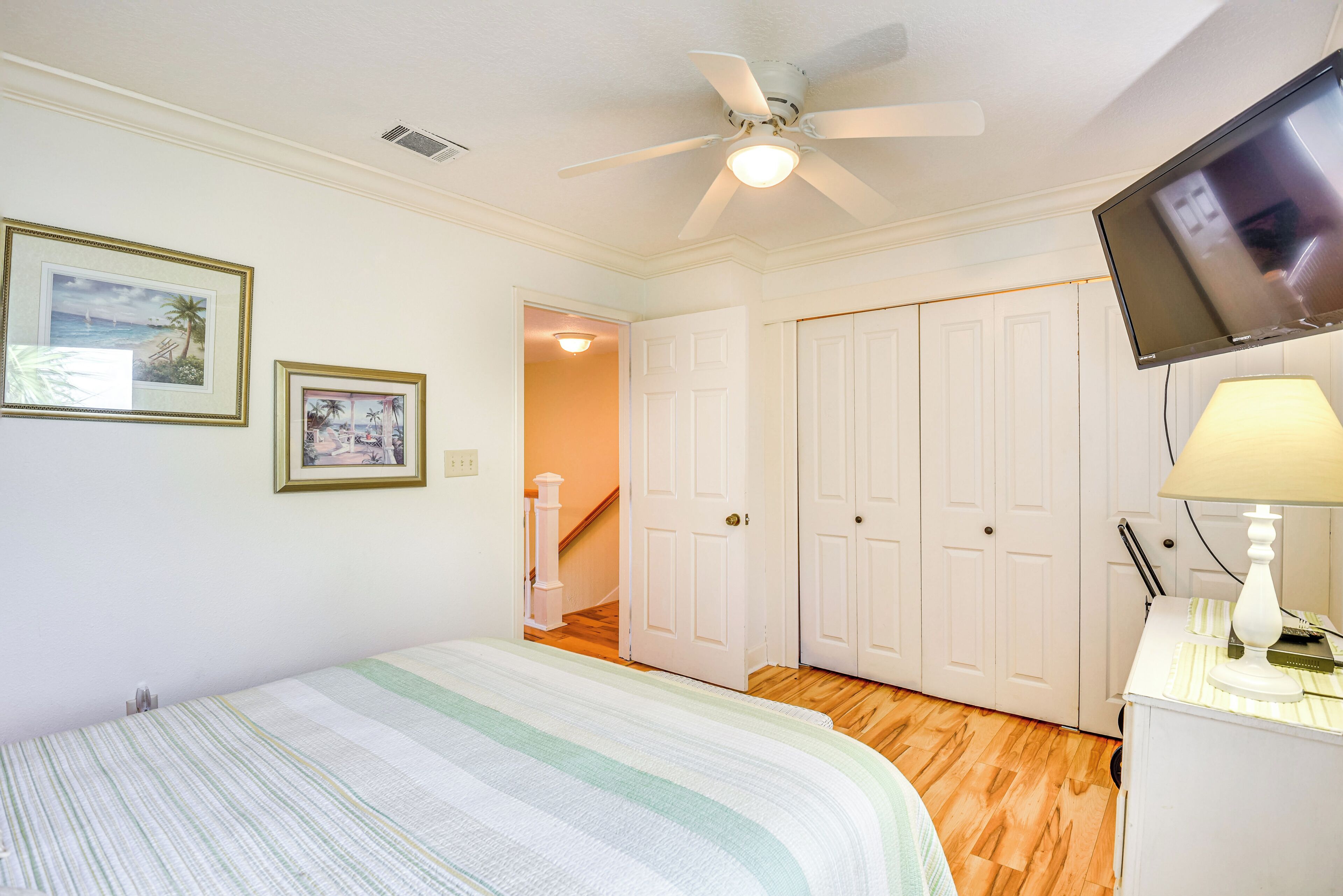 A bedroom with a bed, a ceiling fan, a TV, and a lamp.