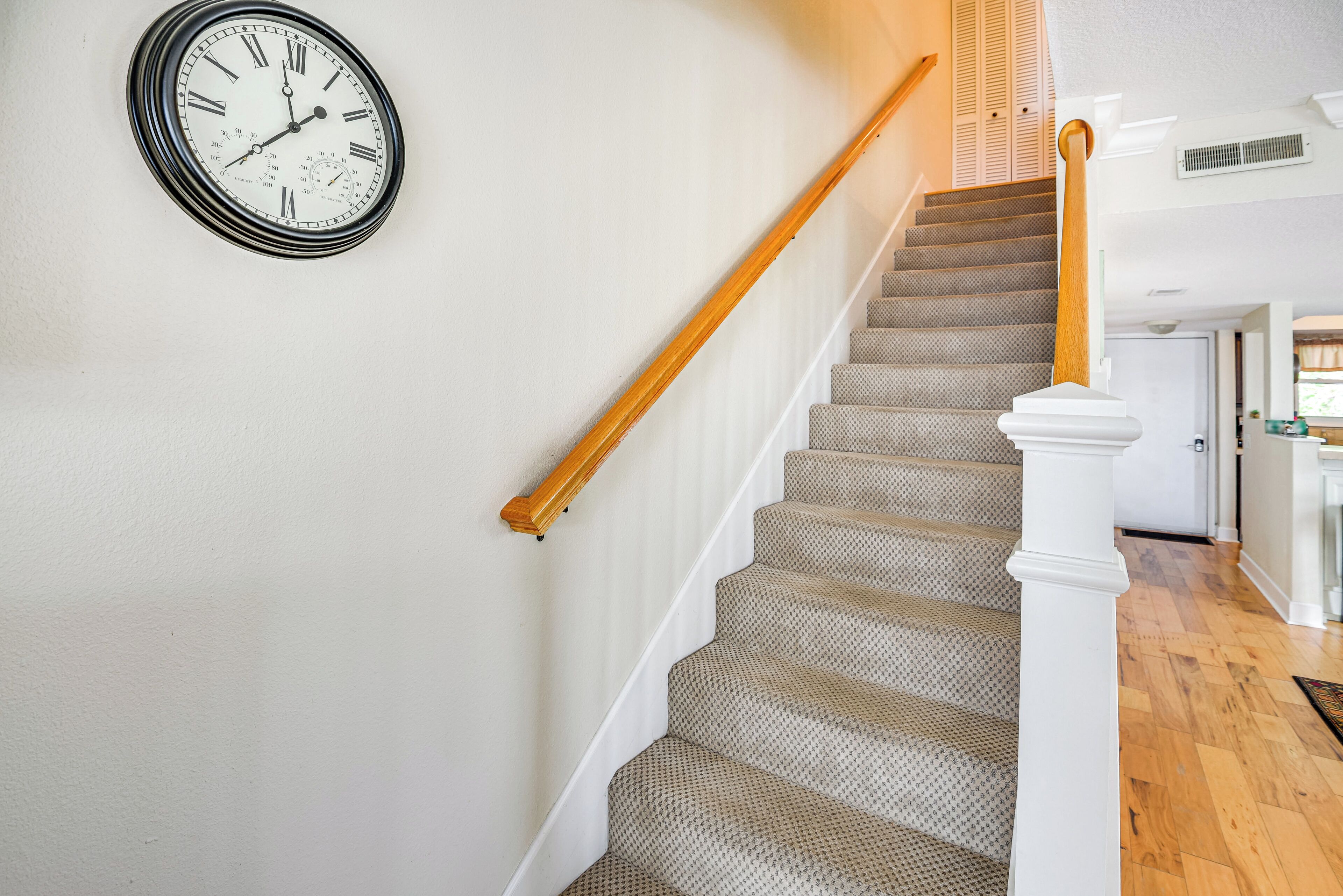 A staircase with a wooden handrail and carpeted steps, leading to a landing with a wall-mounted clock.