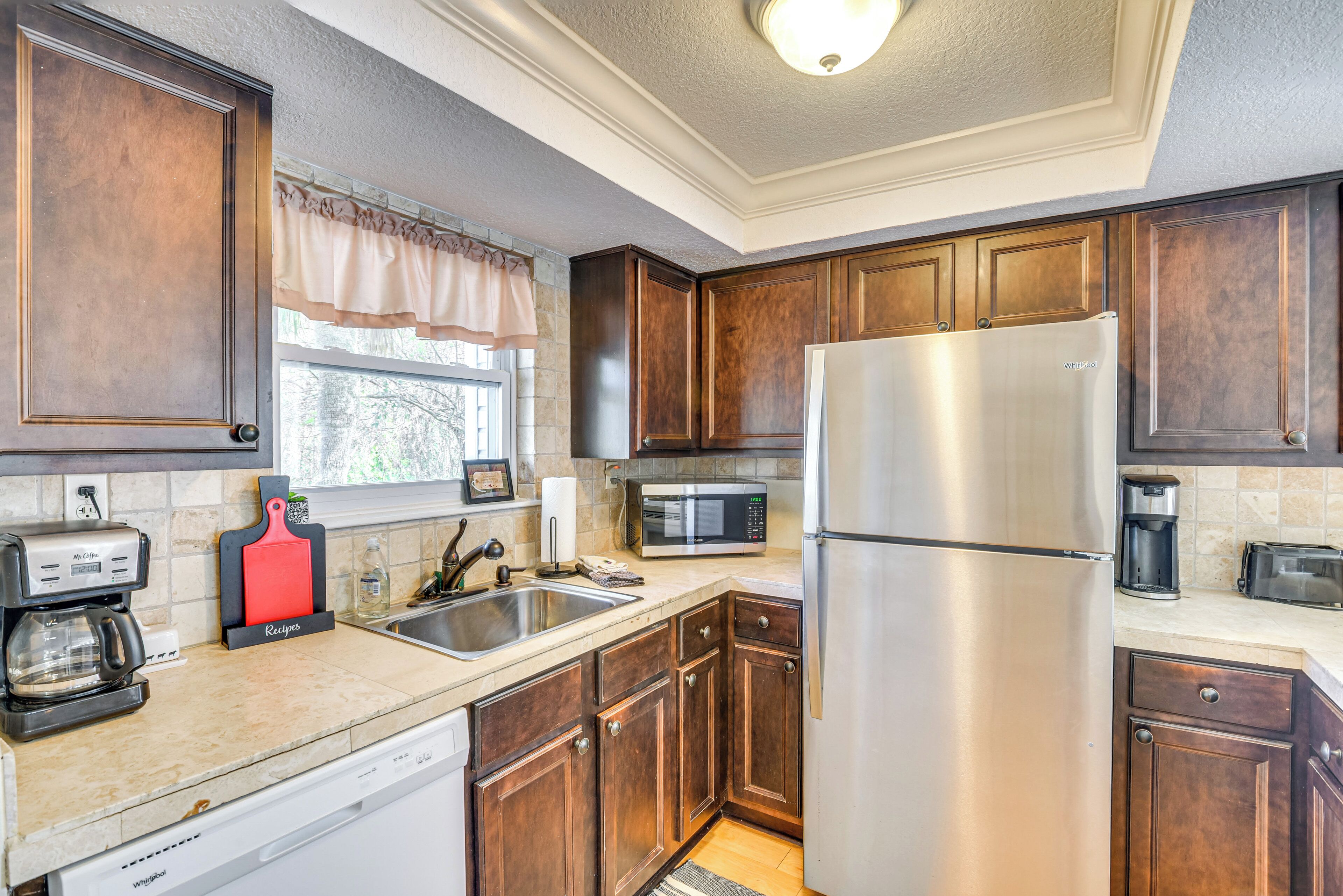 A kitchen with wooden cabinets, stainless steel appliances, a dishwasher, and a window with a curtain.