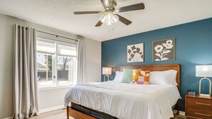 Un dormitorio con cama de madera, ropa de cama blanca, dos lámparas fijadas a la pared y un ventilador de techo.
