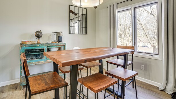 Un comedor con una mesa y sillas de madera, un aparador verde azulado antiguo y un ventanal con cortinas.