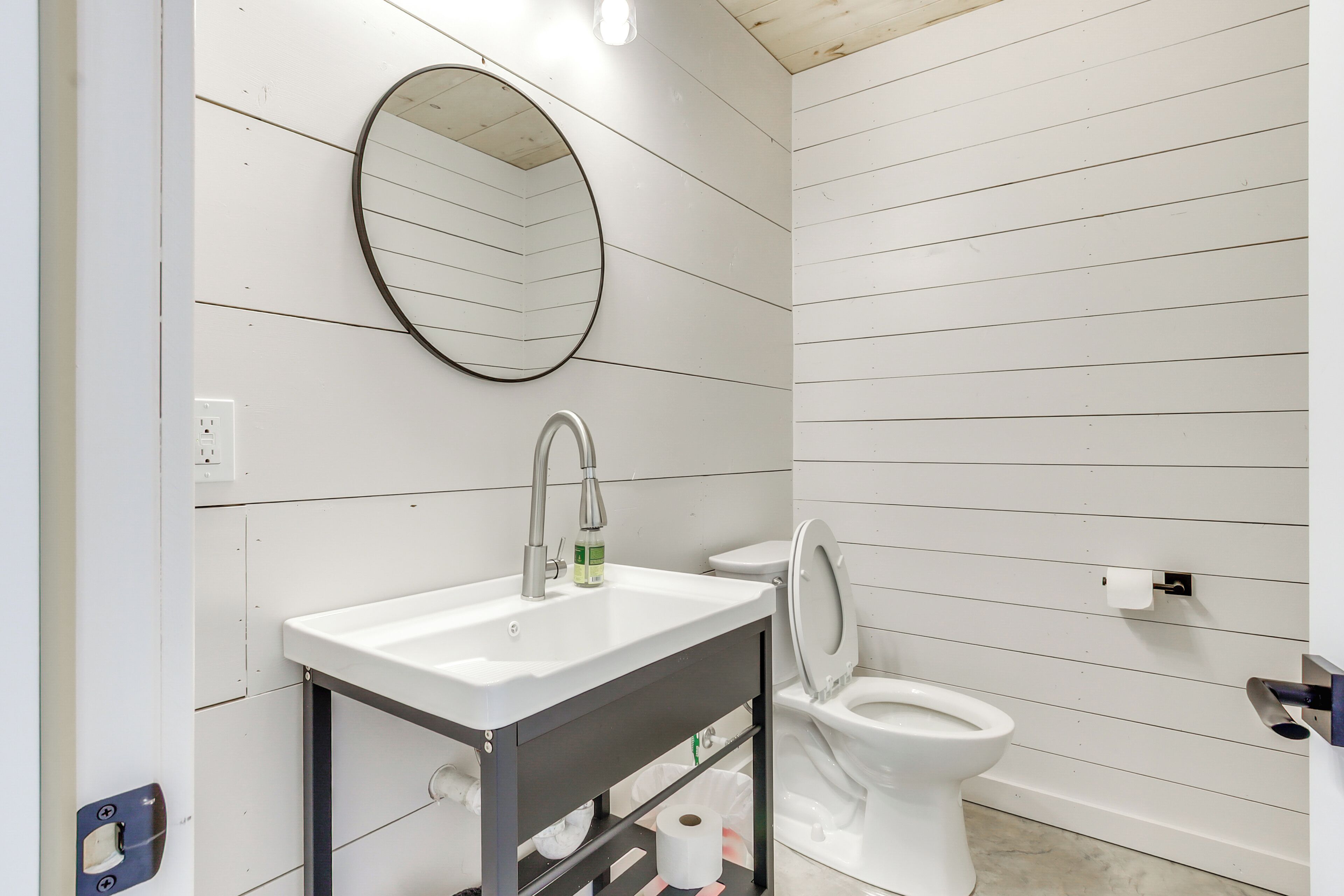 A bathroom with a white sink, a mirror, a toilet, and a shelf with toiletries.