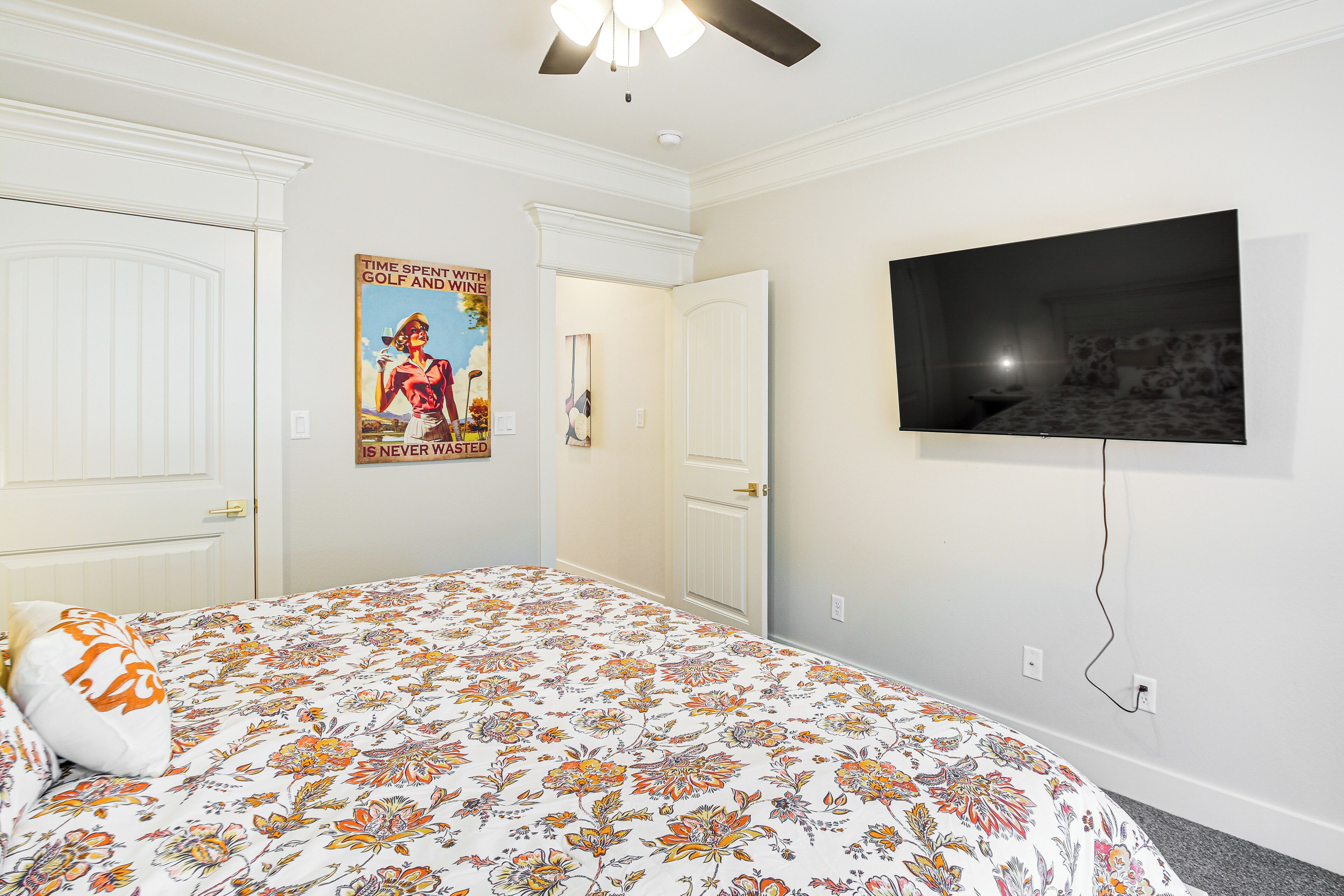 A bedroom with a floral bedspread, a television mounted on the wall, and a door leading to another room.