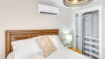 A neatly made bed with white linens and a decorative pillow, a wooden headboard, a bedside table with a lamp, and a built-in closet with sliding doors.