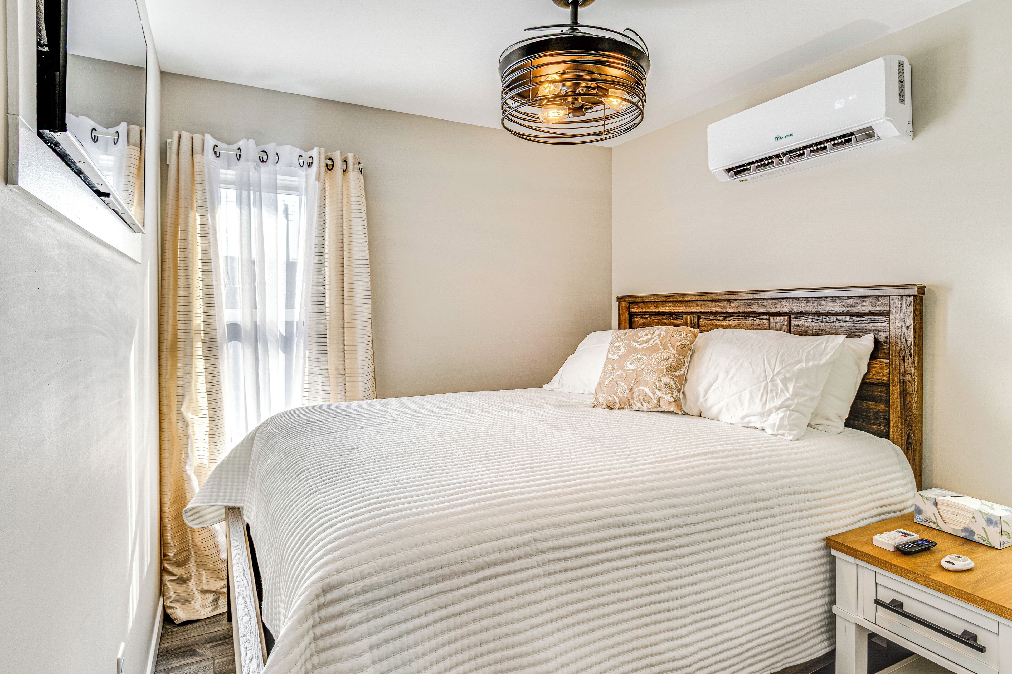 A neatly made bed with a wooden headboard, a bedside table with a lamp, and an air conditioning unit on the wall.