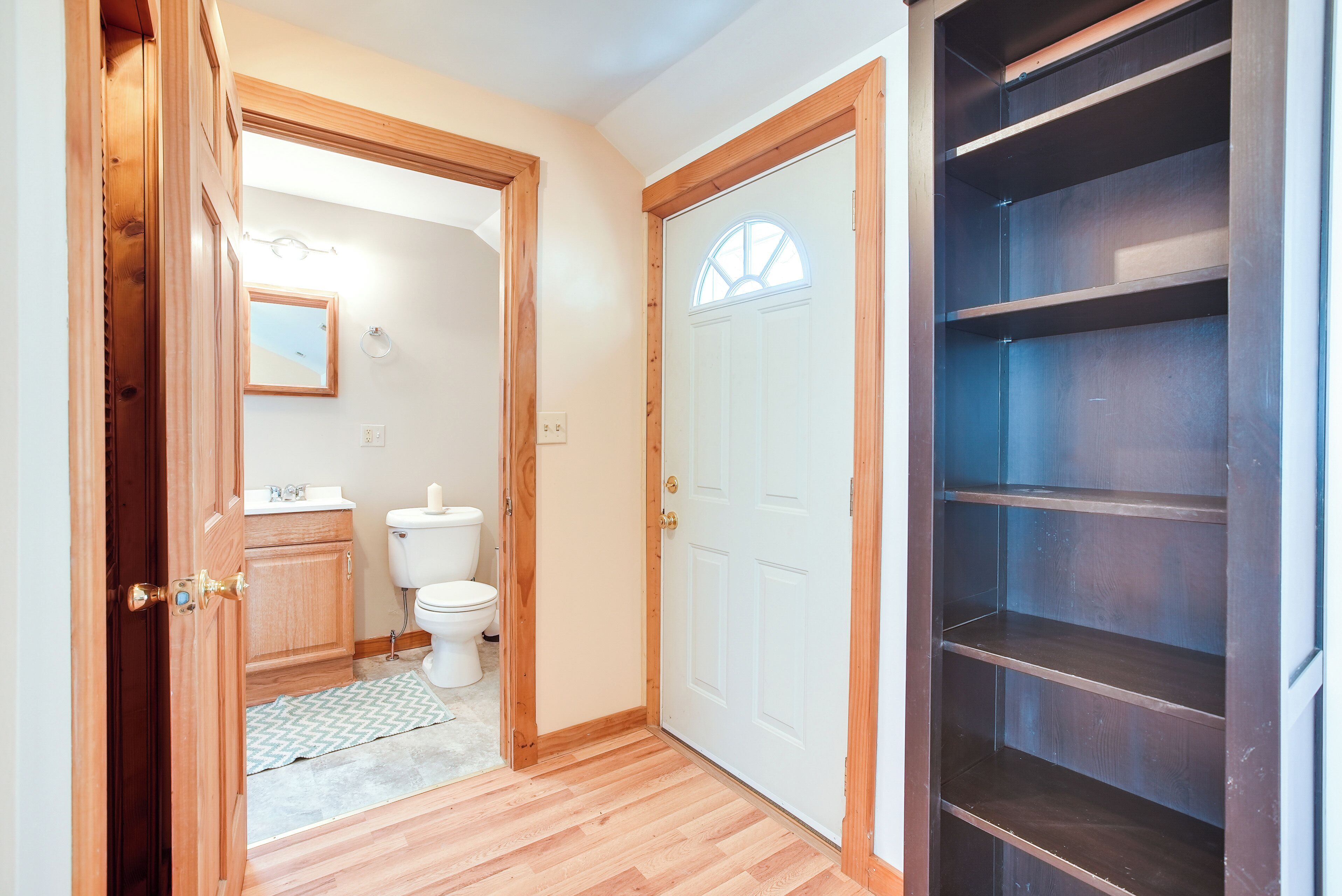 A hallway with a wooden door, a white toilet, and a mirror on the wall.