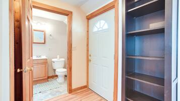 A hallway with a wooden door, a white toilet, and a mirror on the wall.