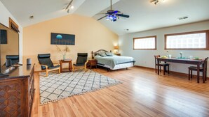 A spacious room with a bed, a desk, two chairs, a wooden floor, a ceiling fan, and a painting on the wall.