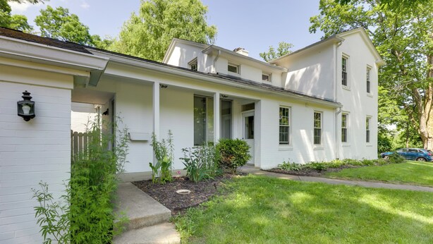 A white two-story house with a front porch, a small garden, and a car parked in the driveway.