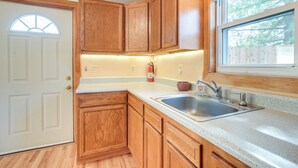 A kitchen with wooden cabinets, a stainless steel sink, and a window with a view of trees.