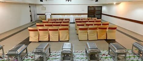 A conference room with rows of chairs, a table, and a row of silver buffet trolleys.