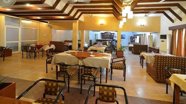 Un restaurant doté de nombreuses tables et chaises, de poutres en bois au plafond et d’un éclairage intérieur chaleureux.