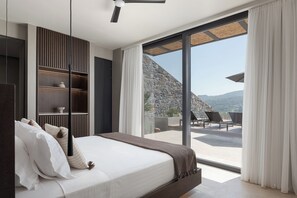 Relax in this serene bedroom with a large bed, shelving unit, and sliding glass door leading to a balcony with a mountain view.